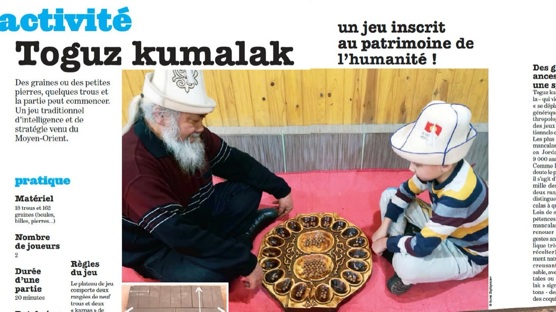 Un homme et un enfant, coiffés du kalpak, jouent au toguz kumalak sur un plateau de bois
